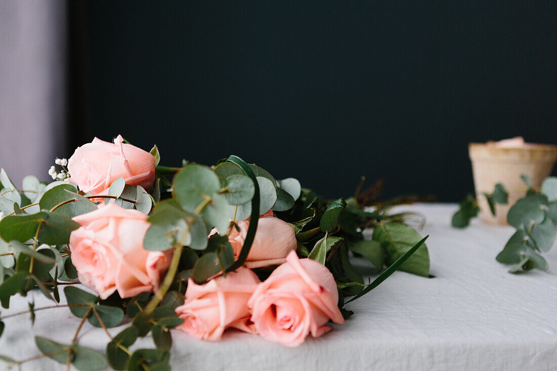 Pink roses bouquet with green leaves lying on white table