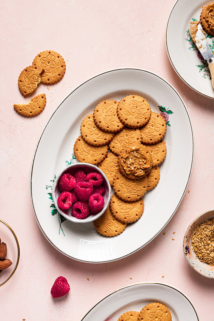 Top view of plates with delicious crispy homemade cookies and fresh raspberries served on table with teapot bowl of seeds