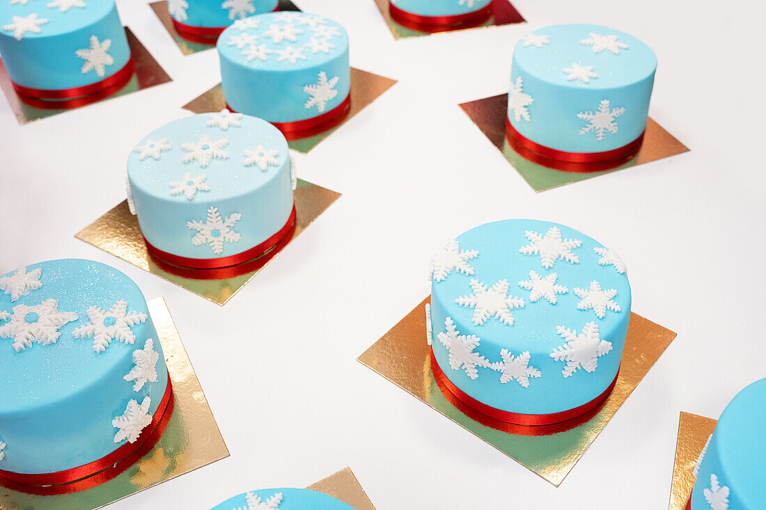 Hoher Winkel von verschiedenen leckeren Winterkuchen mit essbaren Schneeflocken auf goldenen Elementen in einer Bäckerei