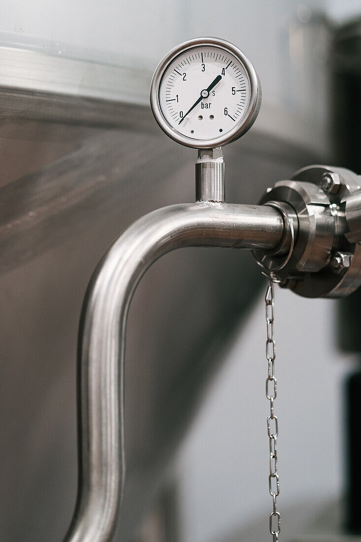 Manometer mit Pfeil und Zahlen auf dem Edelstahlrohr eines professionellen Behälters in einer Bierfabrik