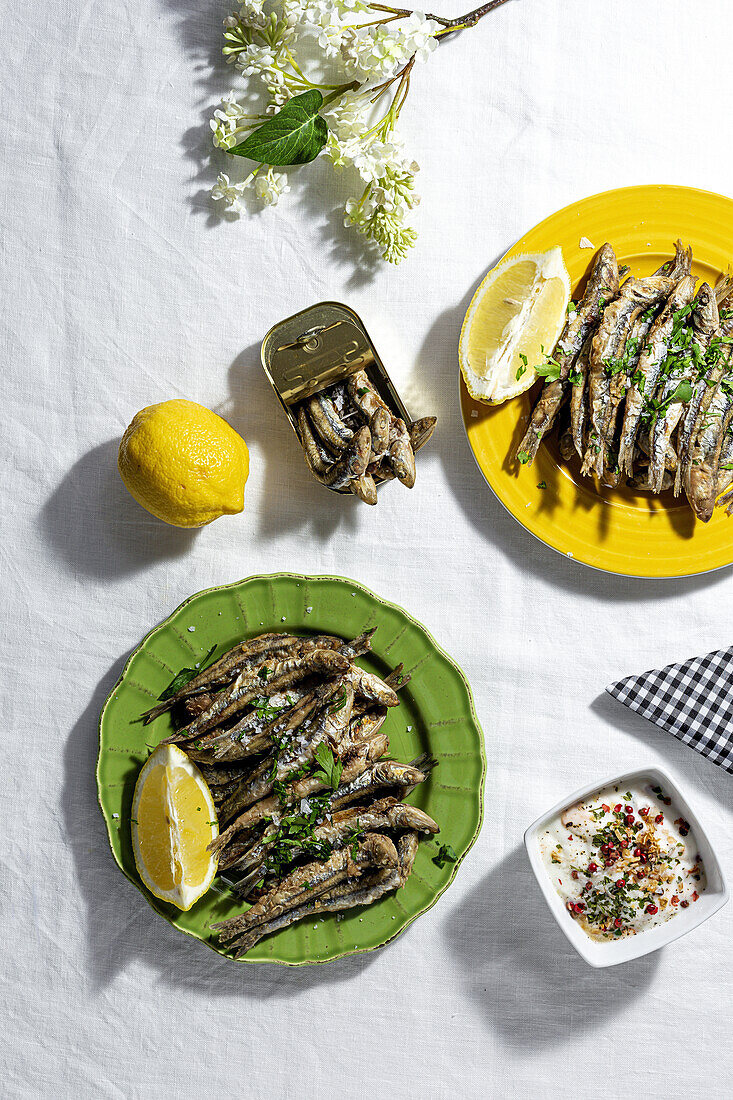 From above of fried and canned anchovies served on table with fresh lemons in restaurant in sunlight