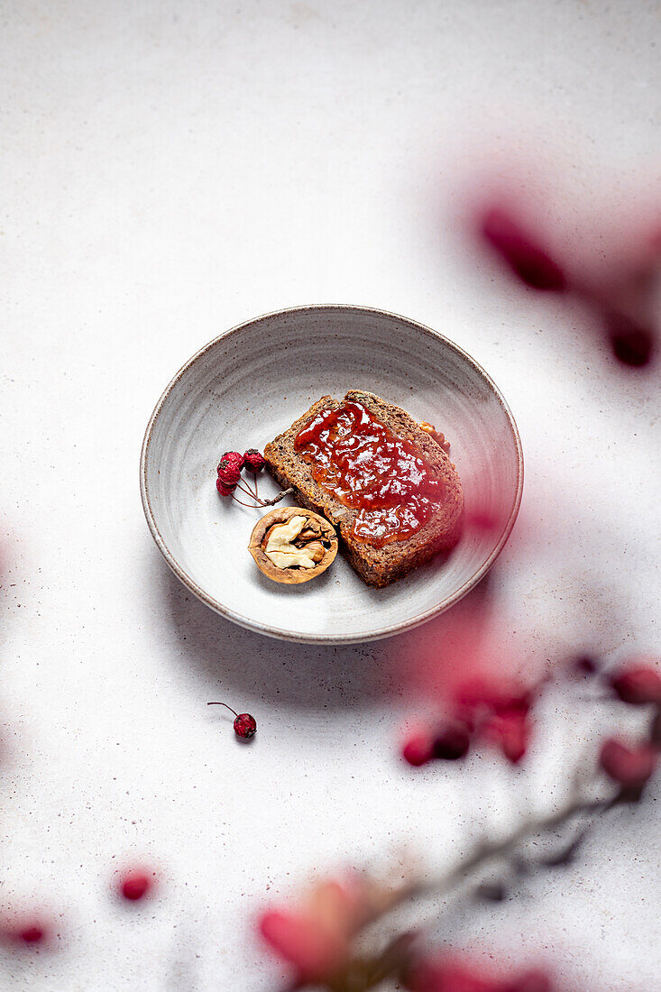 Ansicht von oben von Roggenbrot mit Marmelade neben einer halben Walnuss mit Honig und einem Vogelbeerzweig