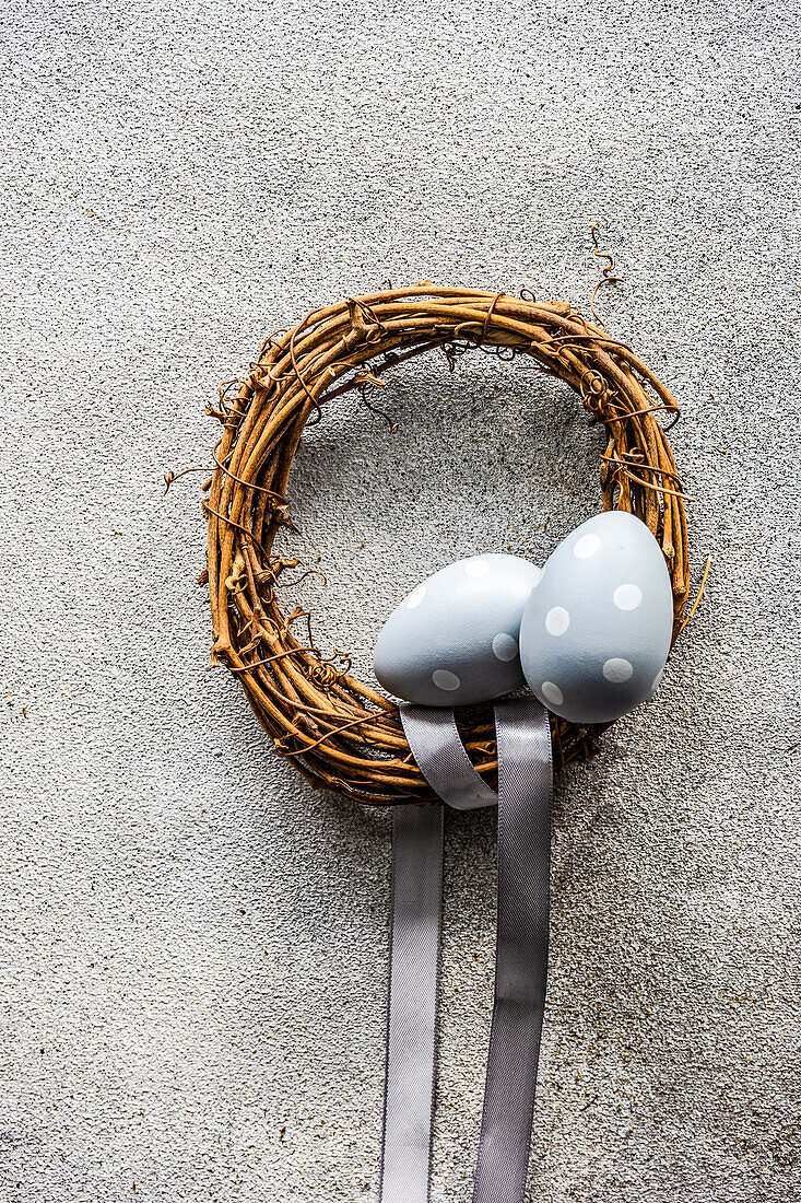 From above easter holiday concept with grape vine wreath decorated with pale blue ribbon on grey concrete background