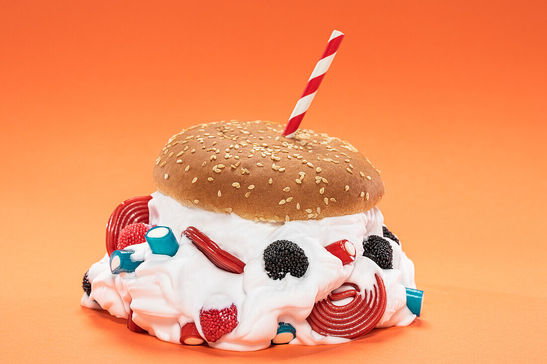 Fresh burger bun filled with sweet whipped cream and assorted jelly candies against orange background