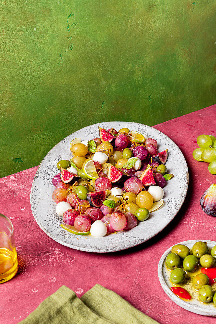 Fresh ripe grapes, olives, figs and mozzarella seasonal christmas salad placed on plate on green and pink tabletop background