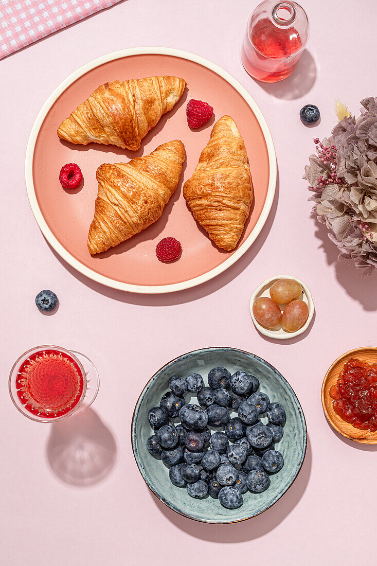 From above of composition of plated with fresh baked sweet croissants served with berries and jam placed on pink table