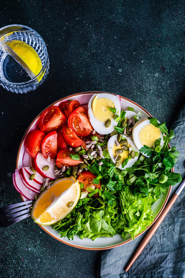 Gesunder Rohkostsalat mit Samen und gekochten Eiern in einer Schüssel auf einem Betontisch serviert