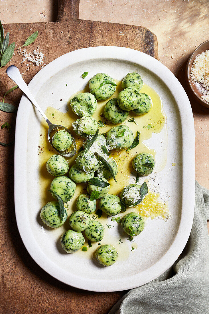 Top view of delicious Italian healthy potato spinach gnocchi served on big ceramic oval plate placed on wooden board