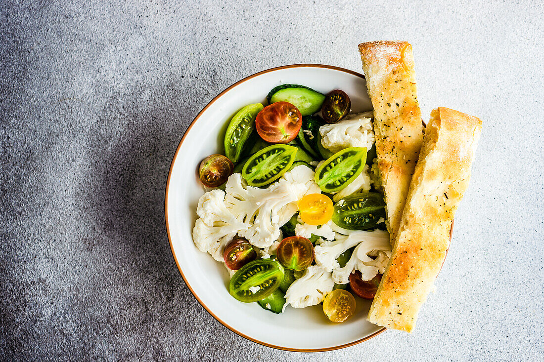 Healthy vegetable salad in the bowl and fresh baked focaccia bread served on concrete table