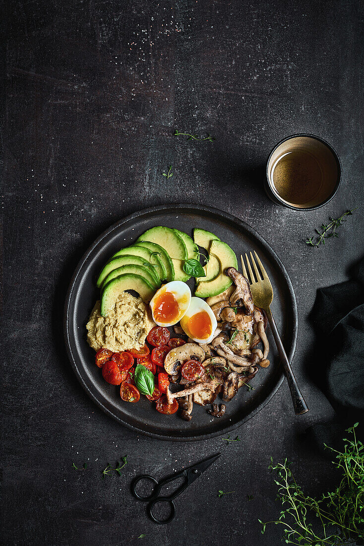 Overhead full plate of delicious dish with hummus from fried champignons and boiled eggs with tomatoes and avocado served fresh leaves of basil