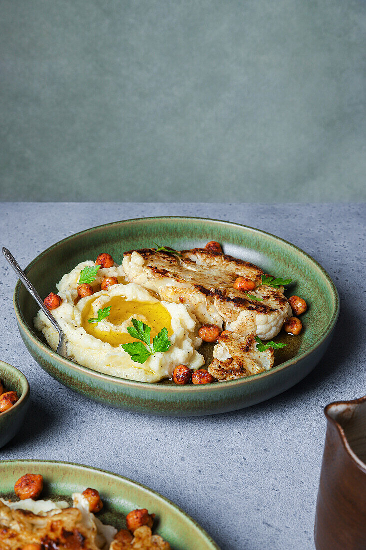 Delicious roasted cauliflower with mashed potatoes and spiced harissa chickpeas served on ceramic plate on gray table background