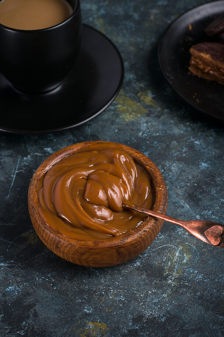 Draufsicht auf Dulce de Leche in brauner Schale mit schwarzer Tasse und Untertasse neben Schokoladen-Alfajores