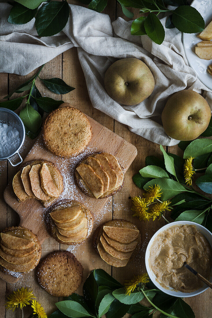 Sweet cookies with slices of apples placed on table and cutting board near dandelions