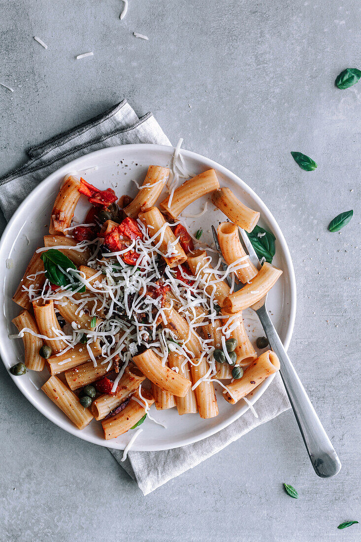 Draufsicht auf ein köstliches Gericht mit Makkaroni-Pasta alla Puttanesca auf einem grauen, rustikalen Tisch