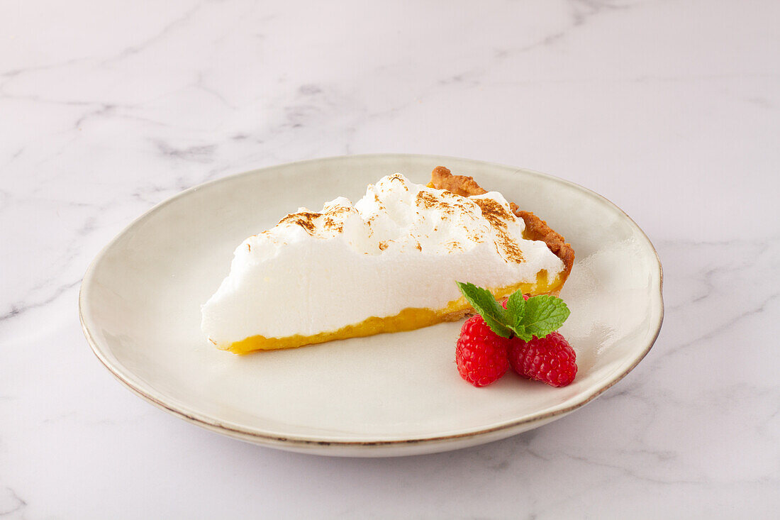 High angle of lemon meringue tart served on plate near ripe strawberries on marble table