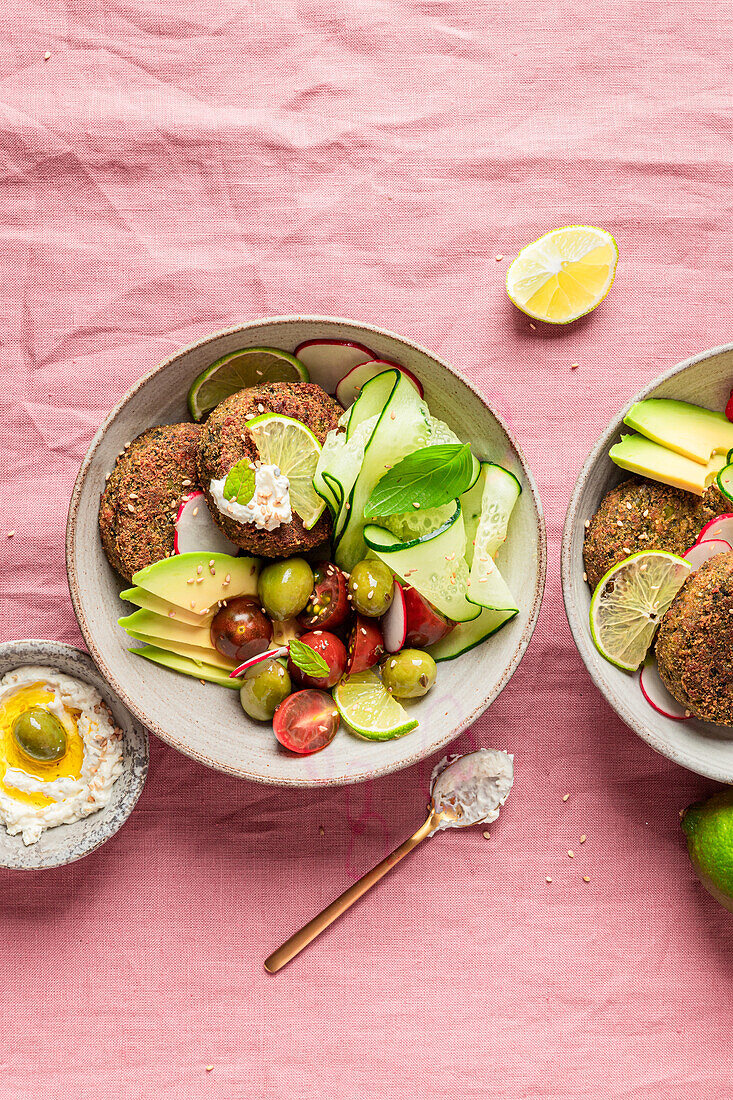 Top view of plate with delicious cream cheese and assorted vegetables placed on napkin near vegan fritters on pink background