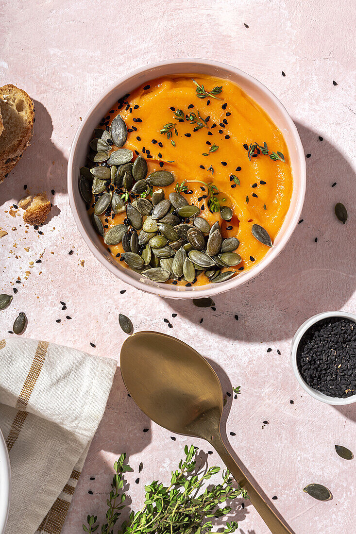 Draufsicht auf appetitliches hausgemachtes Kürbispüree mit Kernen und Kräutern in einer Schüssel auf dem Tisch neben knusprigen Brotscheiben in der Küche