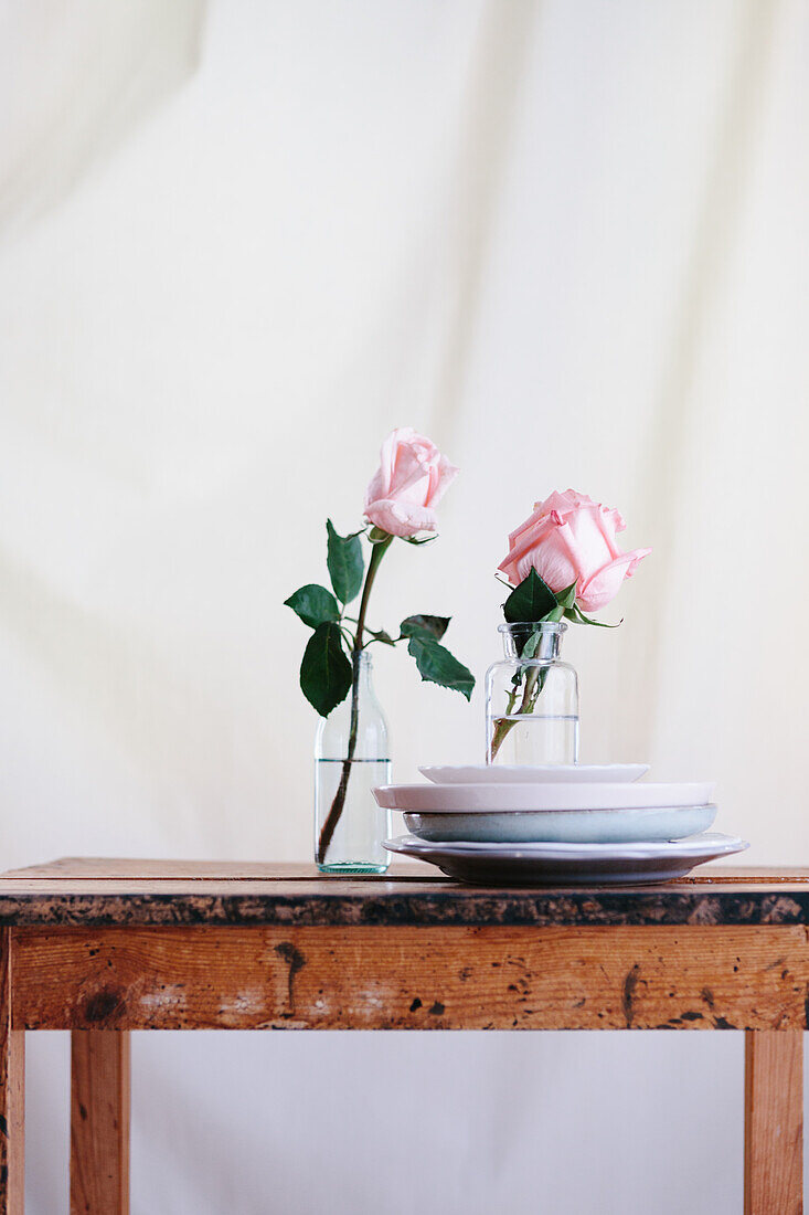 Rosa Rosen in Glasvasen auf einem Holztisch vor neutralem Hintergrund