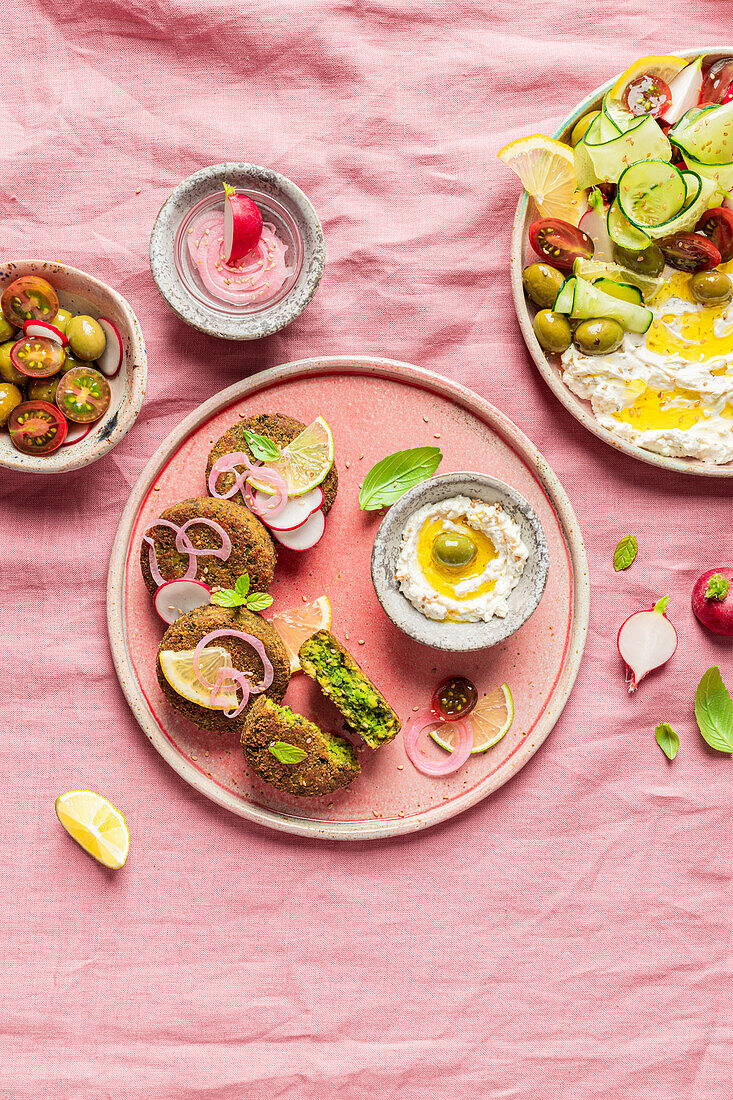 Draufsicht auf einen Teller mit leckerem Frischkäse und verschiedenen Gemüsesorten auf einer Serviette neben veganen Krapfen auf grünem Hintergrund