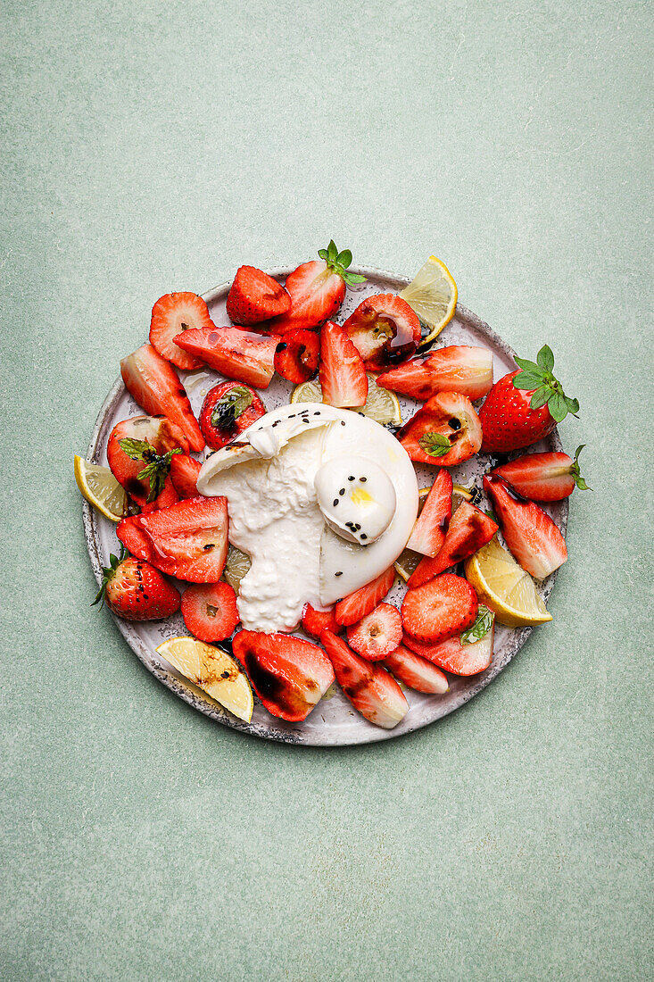 Top view of appetizing fresh strawberries and lemon served with burrata cheese on plate