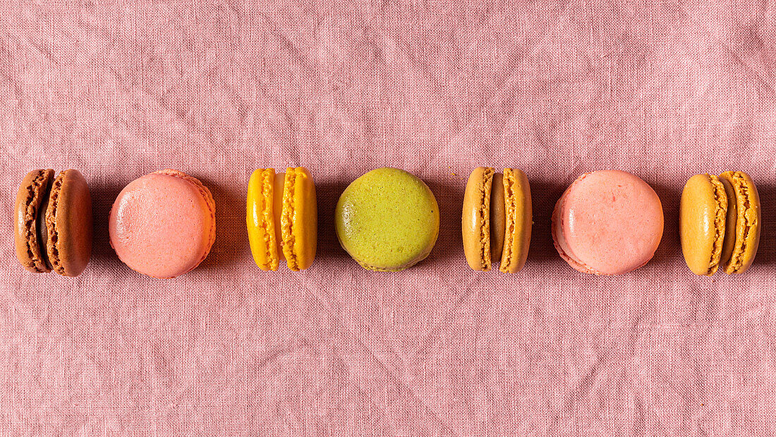 Top view of even row of composed multicolored French macaroons on pink linen tablecloth