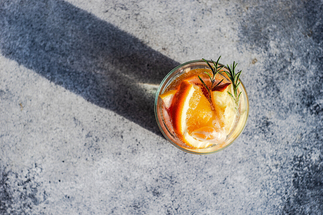 Draufsicht auf einen tropischen Sommercocktail aus Wodka und Sprite mit reifen Früchten und Rosmarin auf grauem Hintergrund