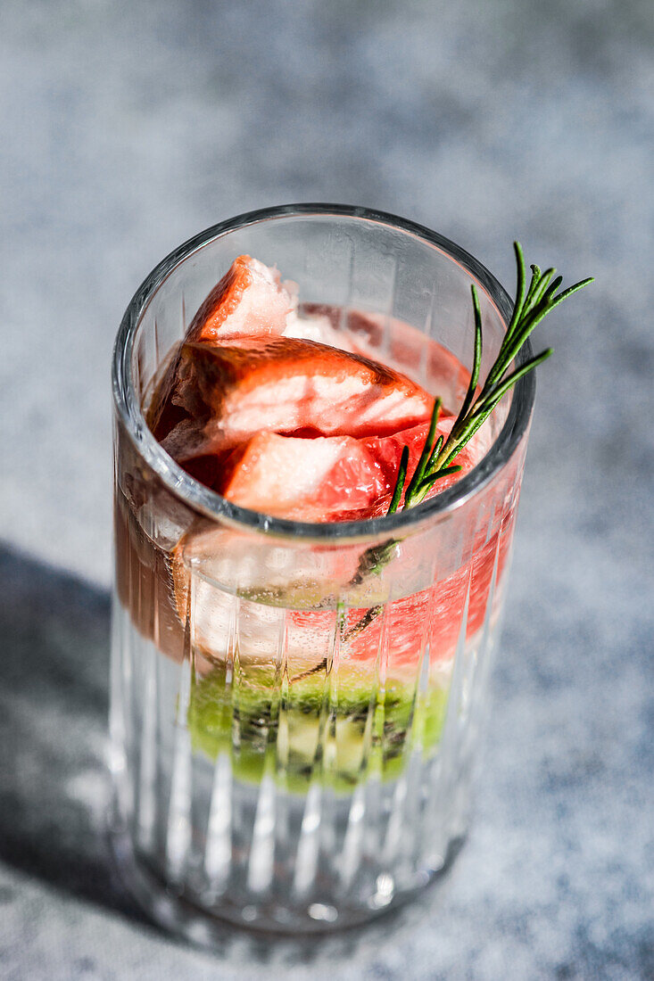 Tropischer Sommercocktail aus Wodka und Sprite mit reifen Früchten und Rosmarin auf grauem Hintergrund