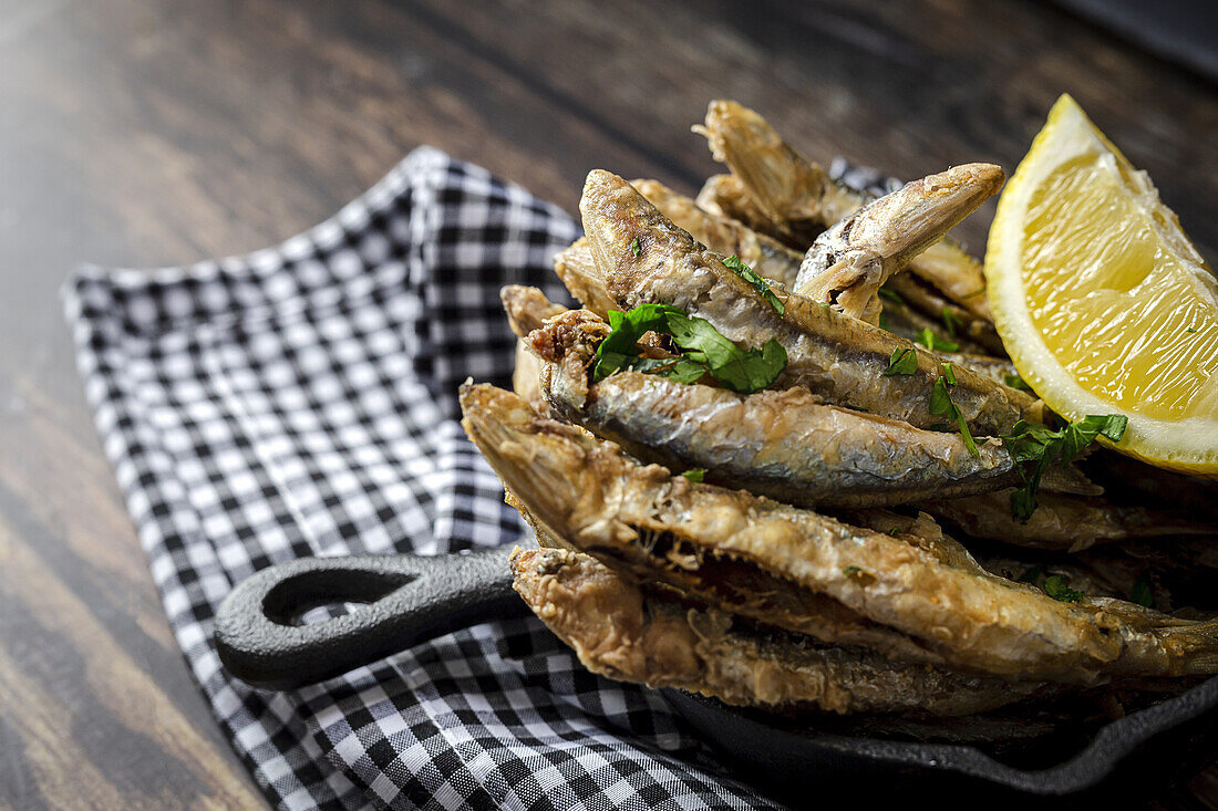 Overhead view of appetizing Fried anchovies with chopped parsley and fresh lemon slice with juicy flesh