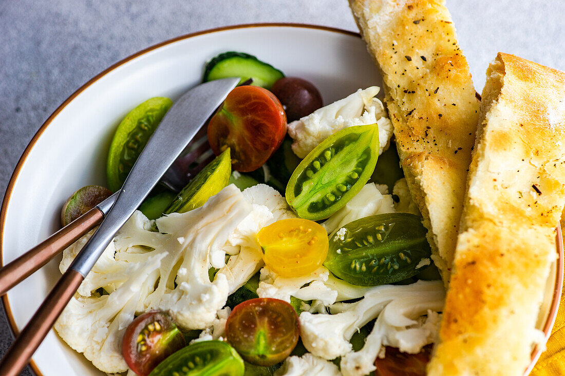 Gesunder Gemüsesalat in einer Schüssel und frisch gebackenes Focaccia-Brot auf einem Betontisch