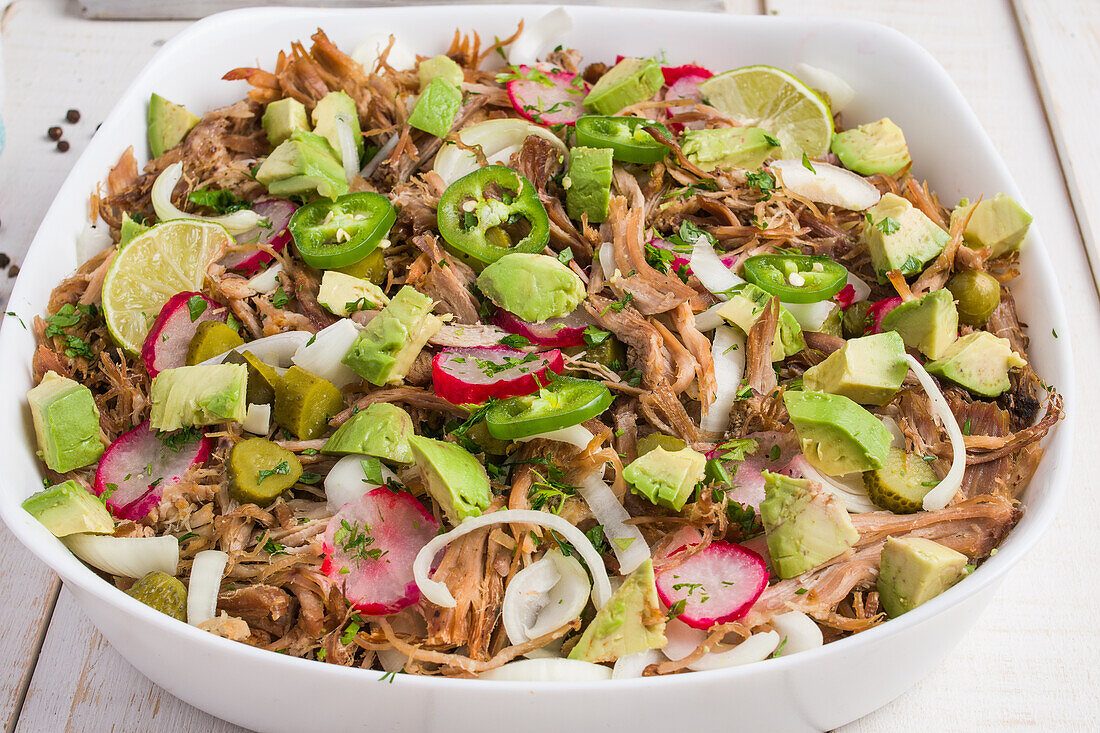 Cuban bowl with pulled meat and chopped avocado with jalapeno and radish and lime served in white ceramic bowl