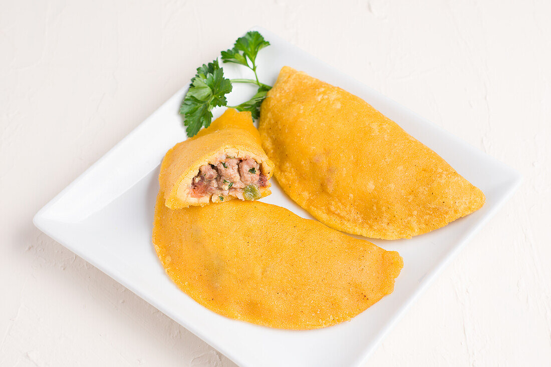 High angle of delicious Colombian patty filled with minced meat on light background stuffed with ground beef and pork with chopped spring onion and fresh coriander on plate