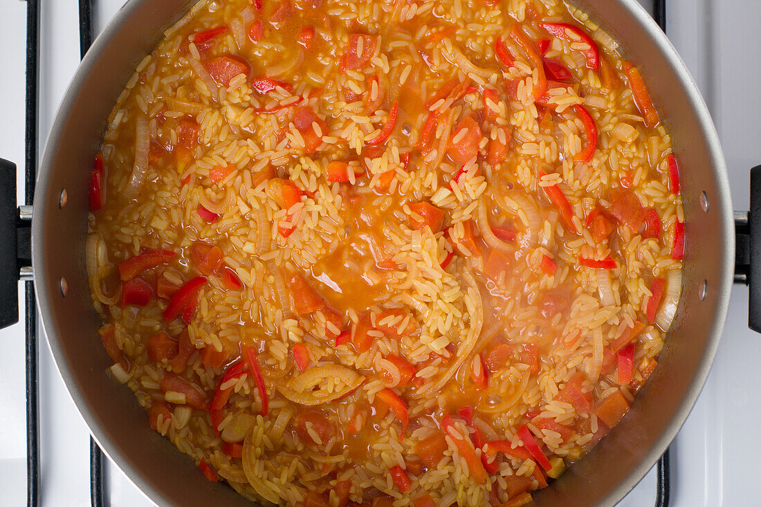 Draufsicht auf gehackte Tomaten und Zwiebeln Valenciana-Reis im Topf, der auf dem Herd für das Mittagessen kocht