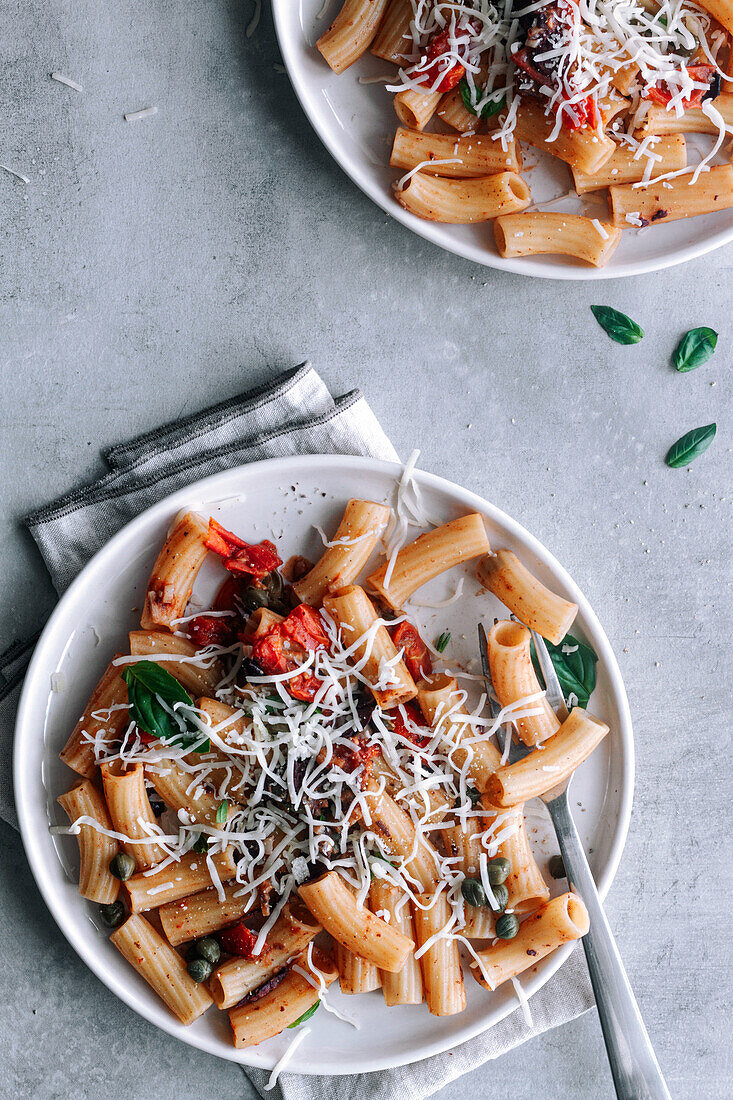 Draufsicht auf ein köstliches Gericht mit Makkaroni-Pasta alla Puttanesca auf einem grauen, rustikalen Tisch