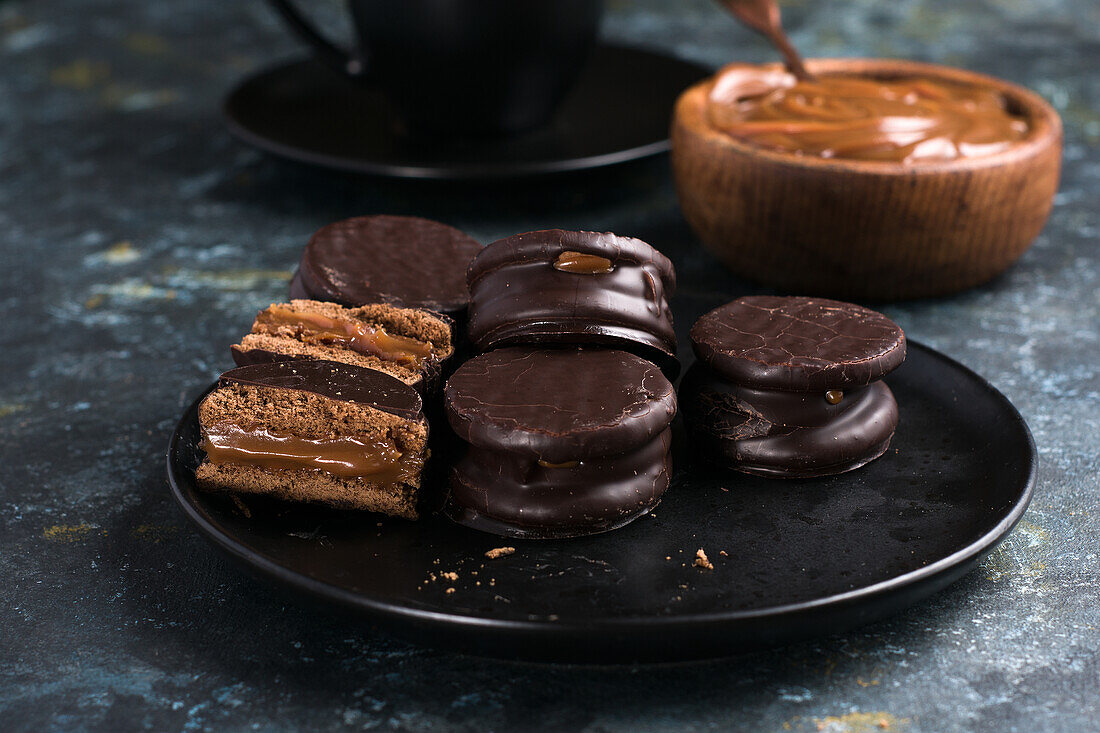 Chocolate alfajores on plate and dulce de leche in bowl placed near cup of hot chocolate