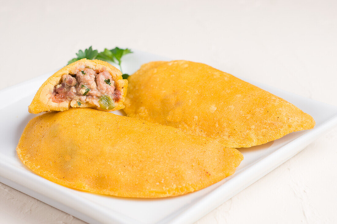 High angle of delicious Colombian patty filled with minced meat on light background stuffed with ground beef and pork with chopped spring onion and fresh coriander on plate