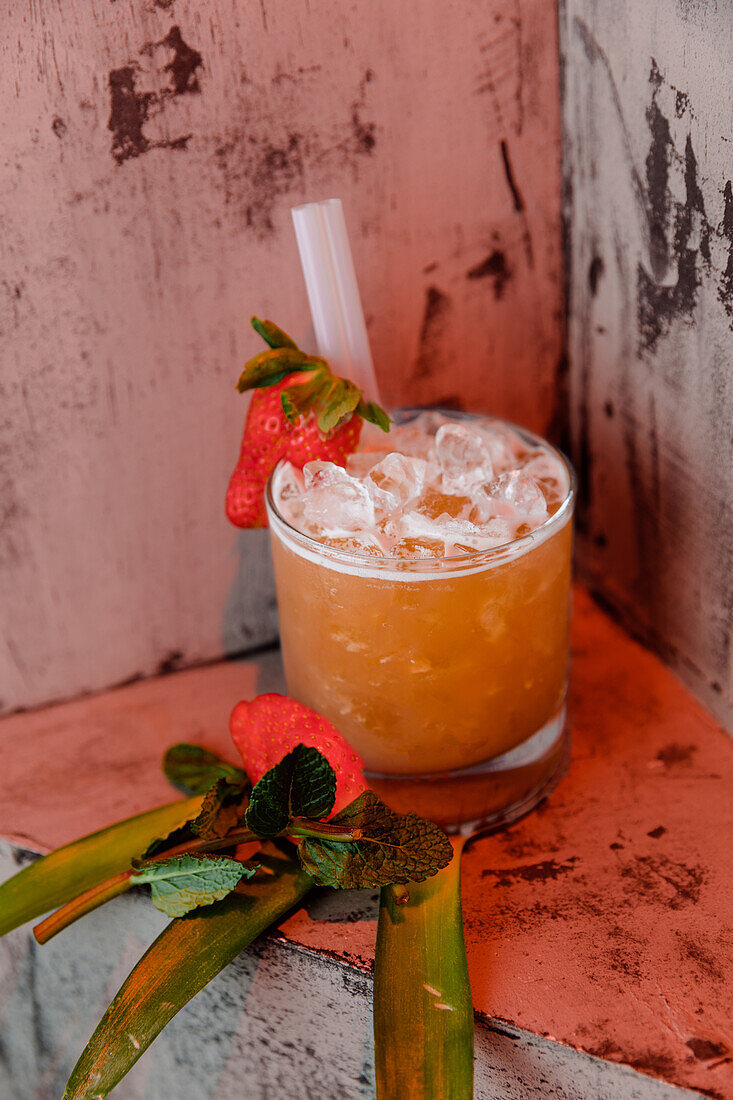 High angle of San Francisco cocktail made of vodka liquor and orange juice garnished with strawberry and ice cubes placed on palm leaves