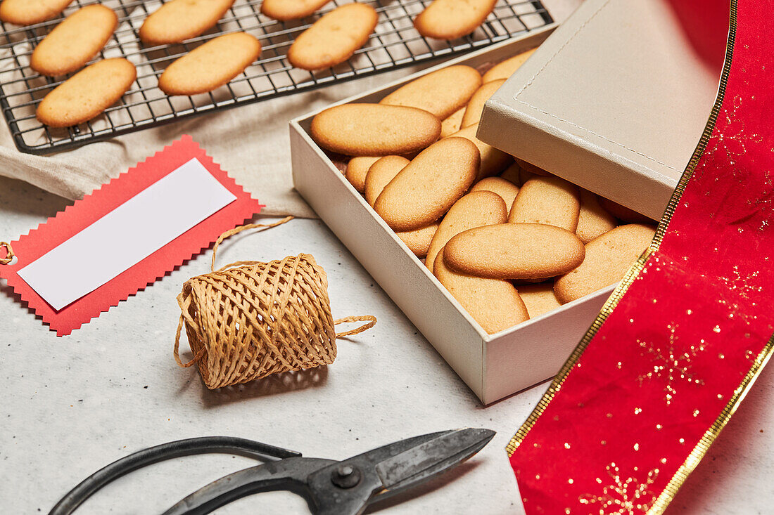 Leckere Weihnachtsplätzchen auf einem Metallnetz und einer Schachtel auf einem Tisch mit verschiedenen Verpackungsmaterialien (von oben)