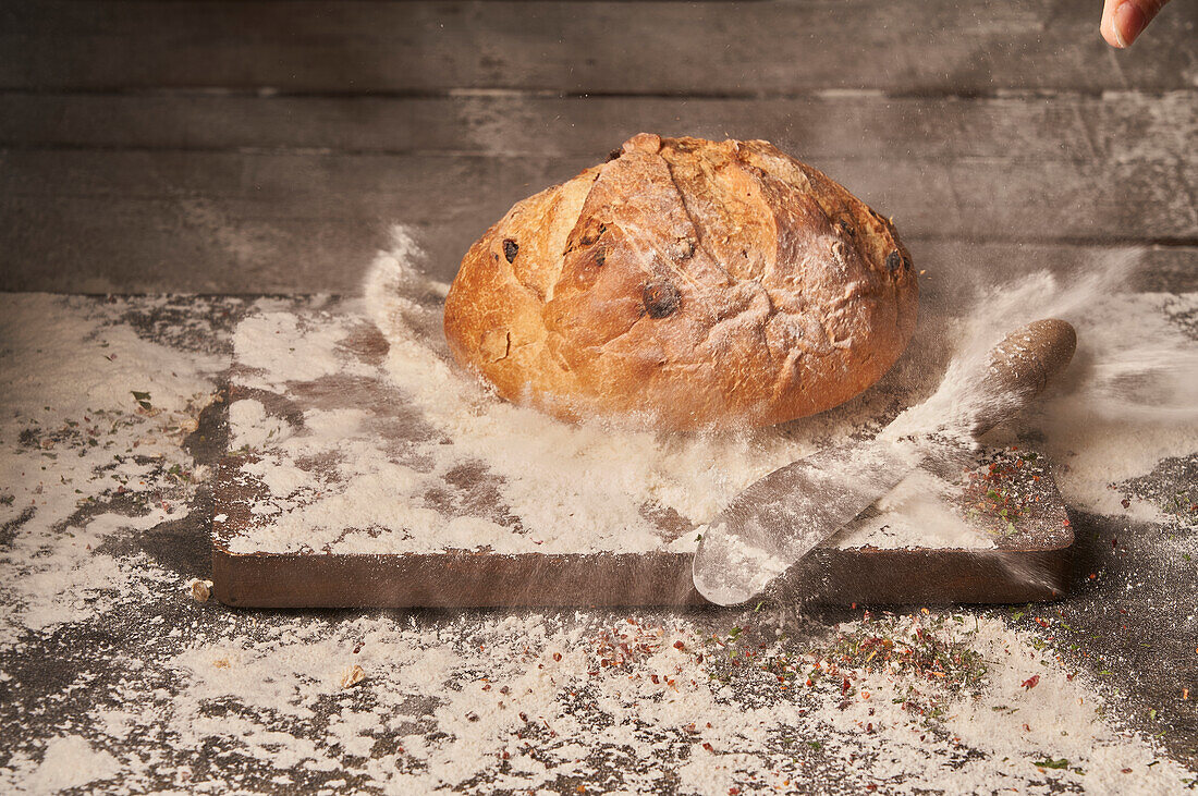 Appetitlich duftendes, frisch gebackenes, hausgemachtes Brot mit Rosinen auf einem mit Mehl bestreuten Holzbrett