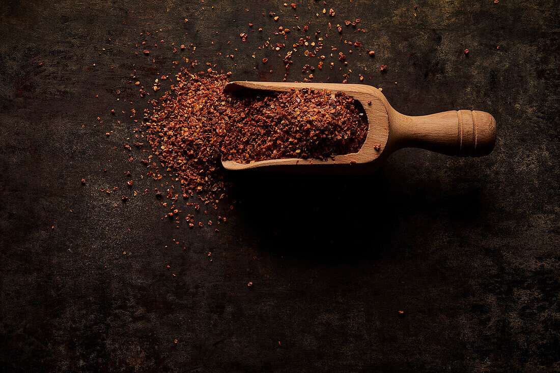Top view of wooden scoop filled with natural aromatic ground sun dried tomato powder on black background