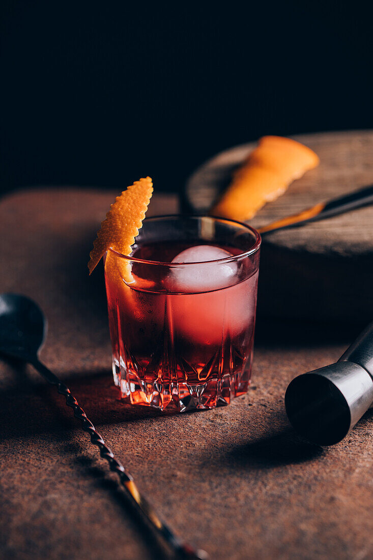 Glas erfrischender alkoholischer Negroni-Cocktail mit Orangenschale garniert und auf dem Tisch inmitten von Barkeeper-Werkzeugen platziert
