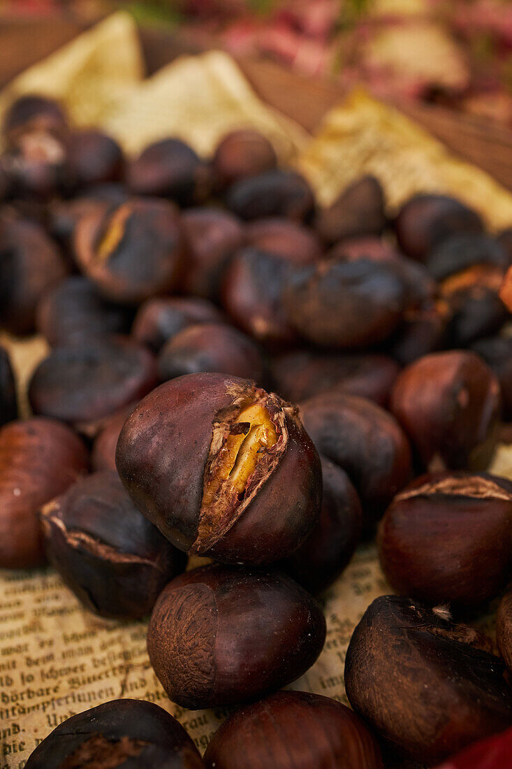 From above close up pile of fresh baked chestnuts on wooden tray near dry leaves on soil in autumn forest