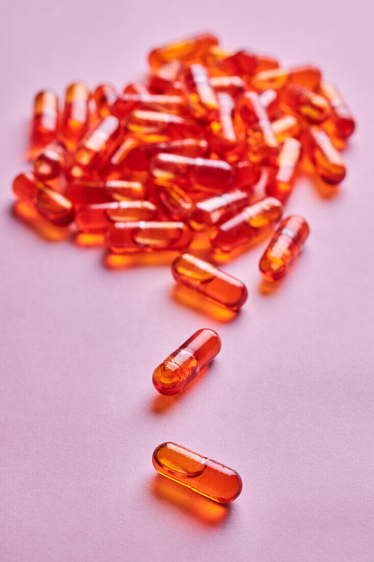 Komposition von orangefarbenen Pillen auf rosa Hintergrund in einem hellen Studio verstreut
