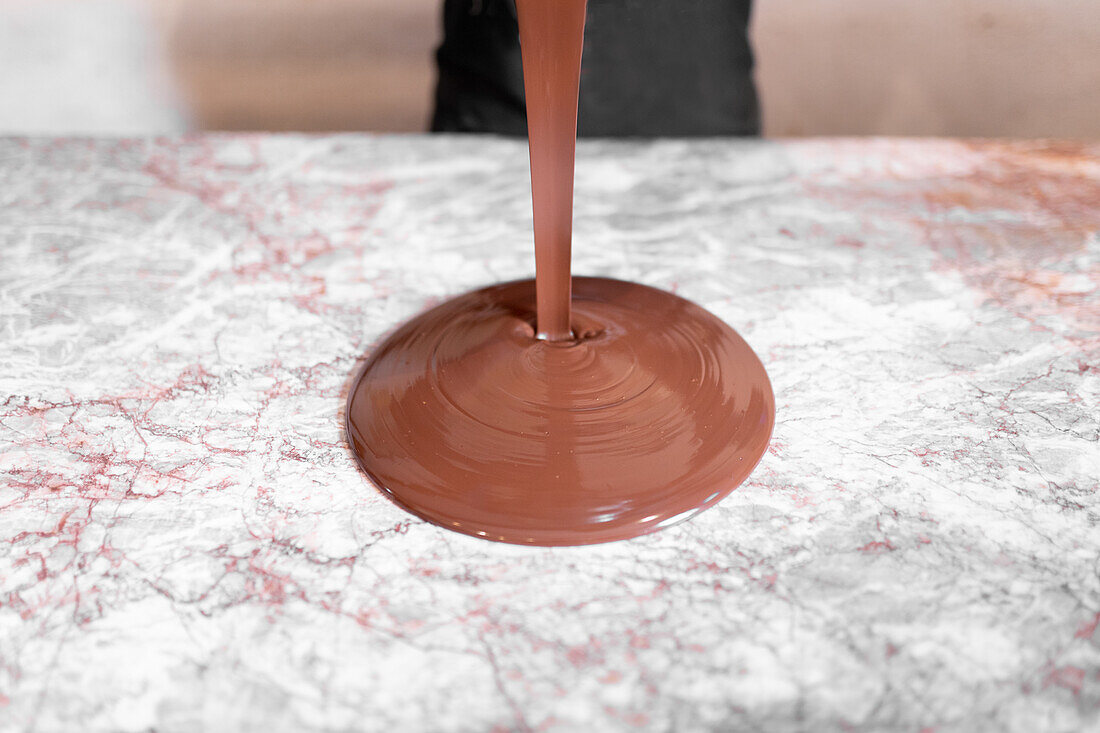 Schokoladenflüssigkeit gießt auf Marmortafel während der Arbeit in der Konditorei