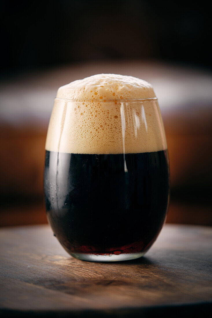 Dark craft beer with foam in glass served on round table in bar