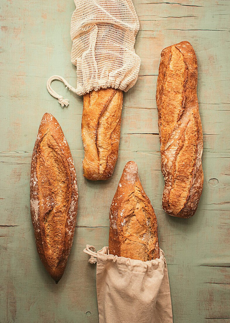 Komposition aus köstlichem, knusprigem Sauerteigbrot, verpackt in Leinensäcken, auf grünem Hintergrund