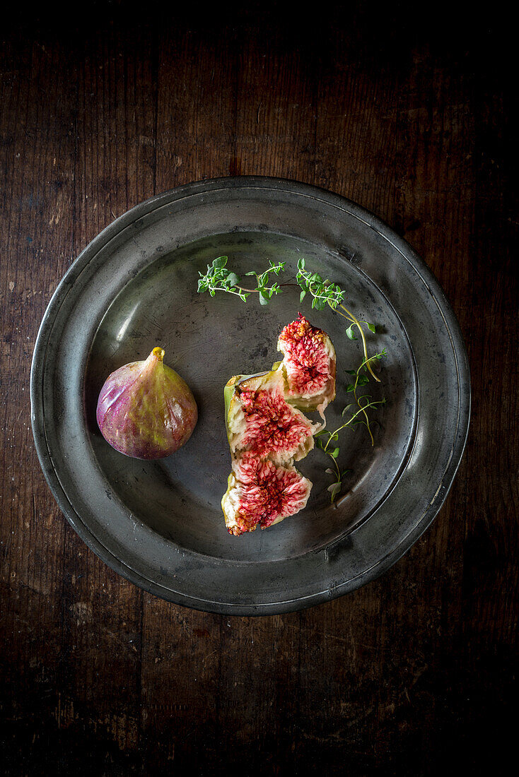 Overhead view of tasty ripe fig slices with aromatic thyme sprigs on plate on wooden surface