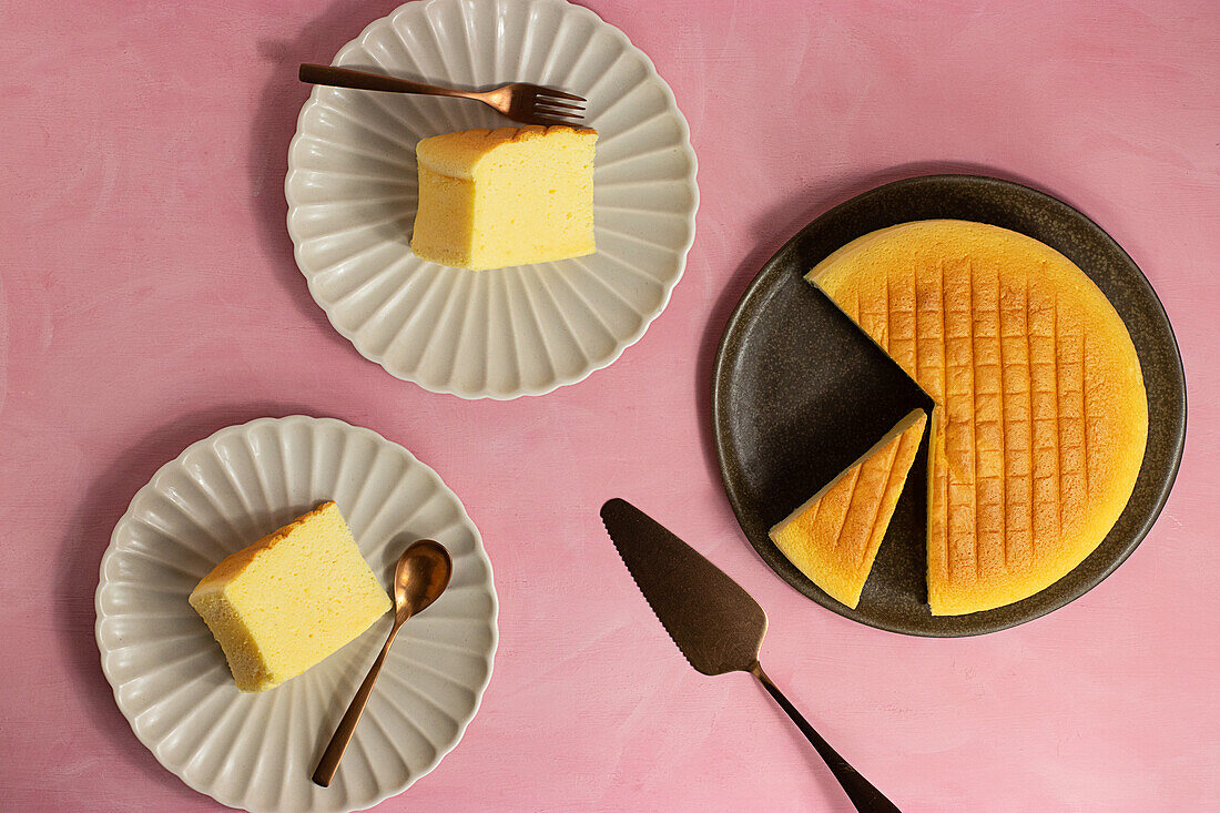 Top view of delicious cotton cheesecake served on plates near spatula on pink background