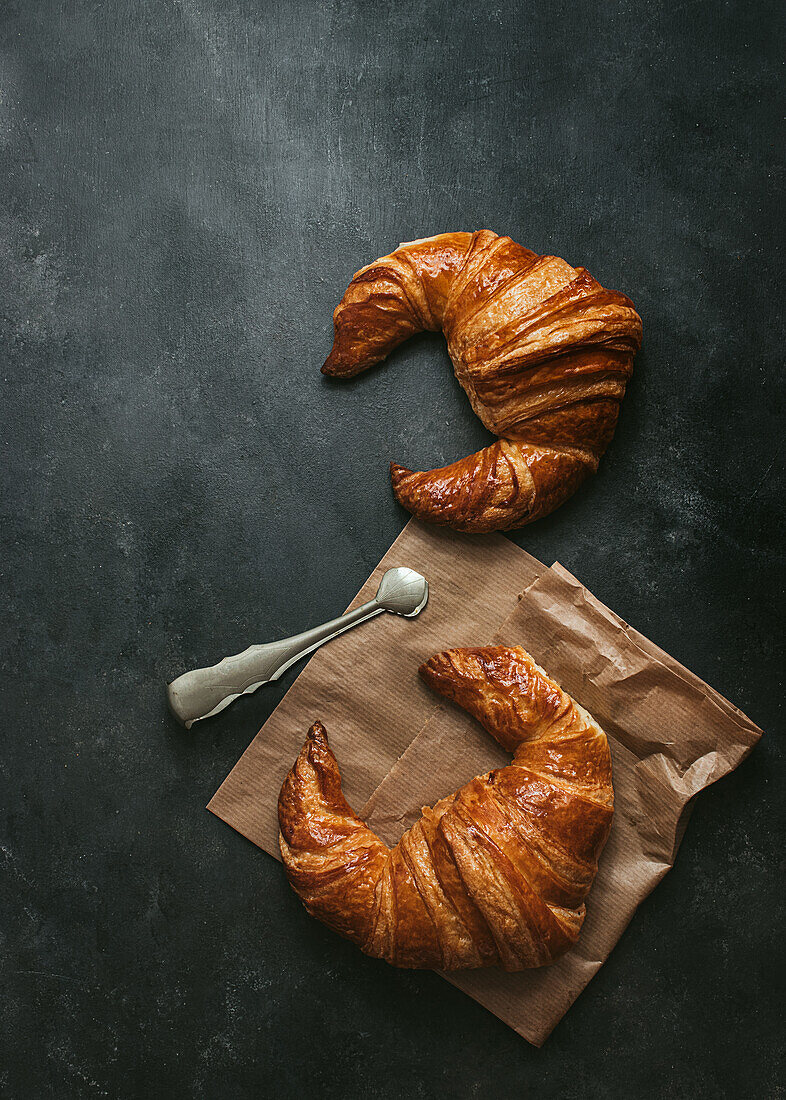 Top view composition with tasty fresh crusty croissants placed with paper bag and metal tongs on black background