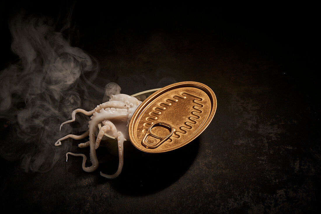 From above of tasty white octopus with tentacles in tin can with opened lid placed on black background with smoke