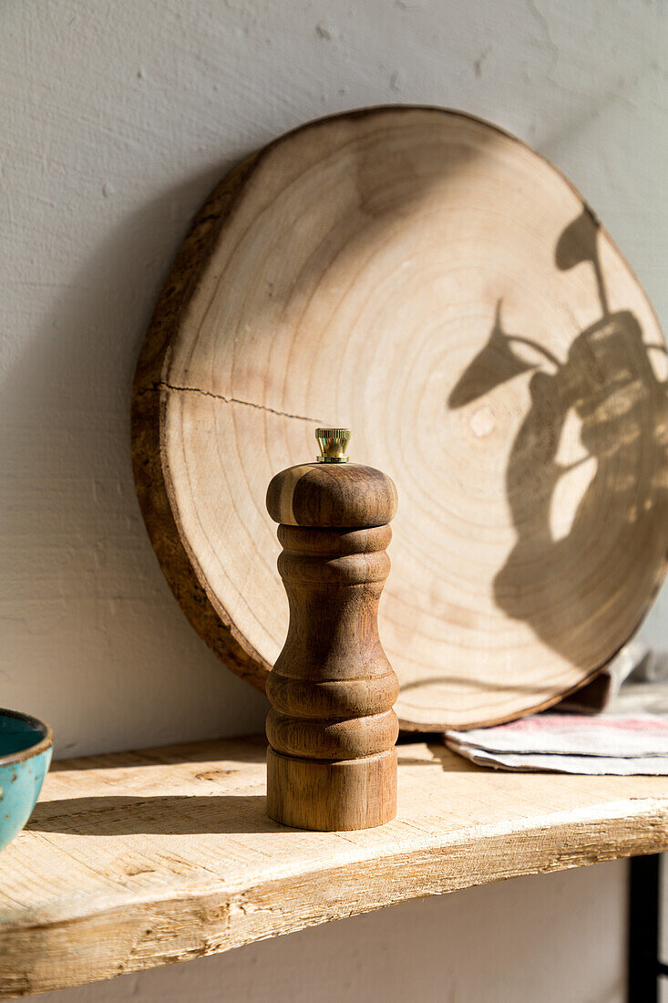 Wooden pepper mill and round board placed on rustic lumber shelf near wall in eco friendly style home kitchen